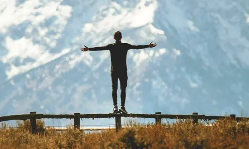 Man standing on fence, arms outstretched